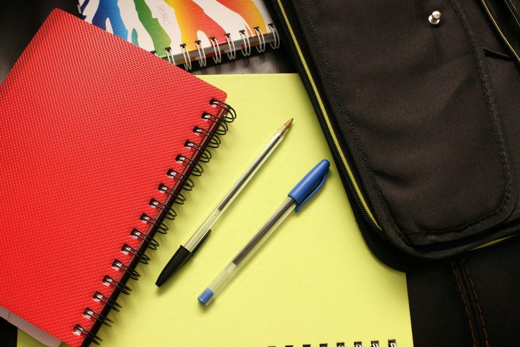 Back-to-school supplies including red notebook, pens, and yellow notepad, symbolizing college preparation and financial planning for education costs.